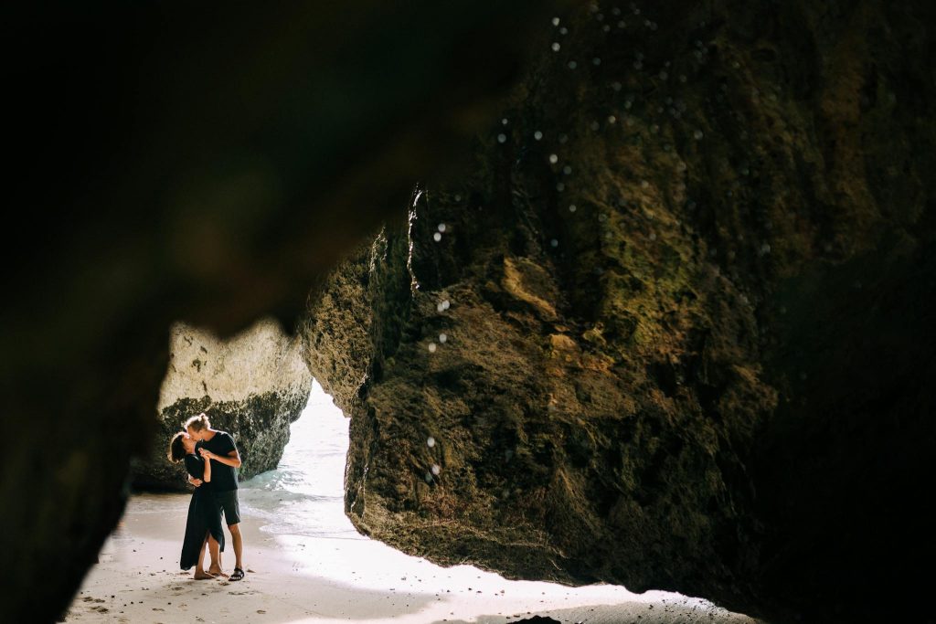 A couple shares a tender moment in the sunlight within a secluded rocky cave.