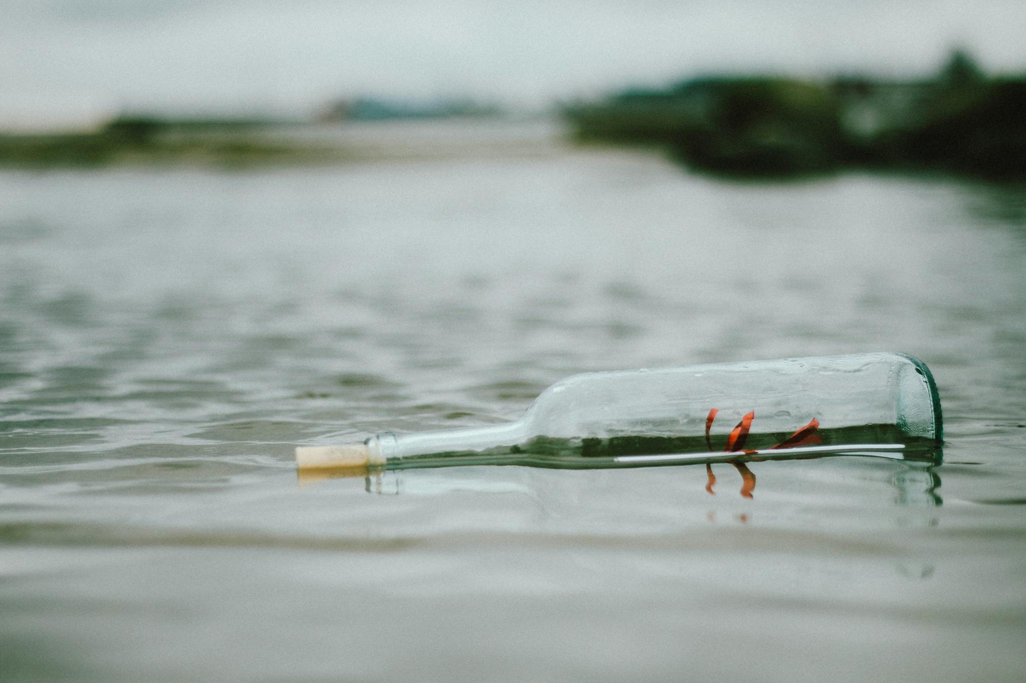 A glass bottle with a letter inside floats on a tranquil water surface, creating a sense of mystery.