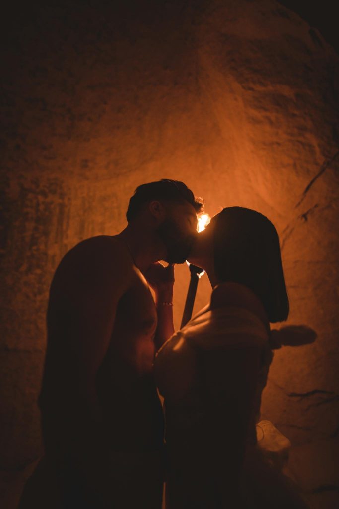 Silhouetted couple sharing a kiss in a dimly lit cave, illuminated by torchlight.
